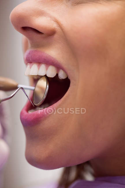Крупный план стоматолога, осматривающего пациентку с помощью инструментов в стоматологической клинике — стоковое фото