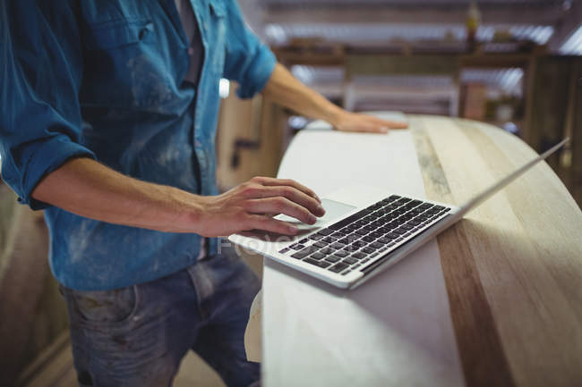 Mid section of man using laptop in surfboard workshop — Stock Photo