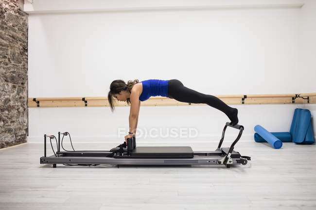 Mujer ejercitándose en equipos de reformador en el gimnasio - foto de stock