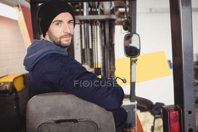 Portrait de mécanicien assis sur un chariot élévateur dans un garage de réparation — Photo de stock