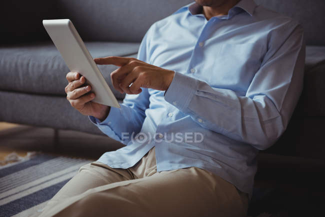 Sección media del hombre usando tableta digital en la sala de estar en casa - foto de stock