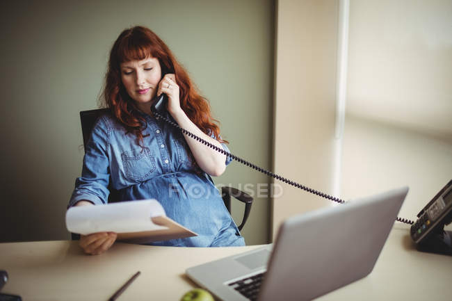 Femme d'affaires enceinte parlant au téléphone pendant qu'elle travaillait au bureau — Photo de stock