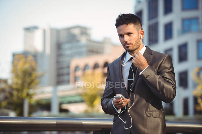 Homme d'affaires écoutant de la musique sur un téléphone portable près d'un immeuble de bureaux — Photo de stock