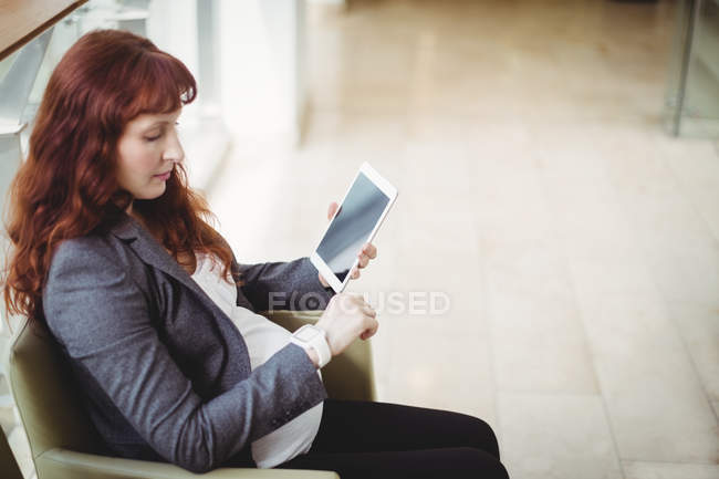 Беременная деловая женщина с цифровым планшетом рядом с коридором в офисе — стоковое фото