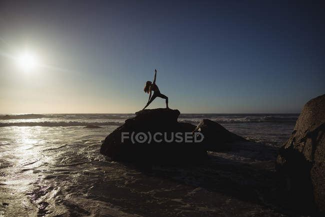 Mujer realizando yoga sobre roca al atardecer - foto de stock