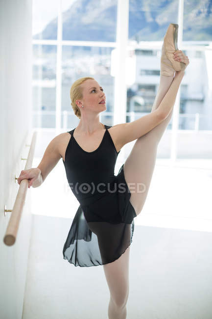 Балерина растягивается на барре во время репетиции балетных танцев в студии — стоковое фото