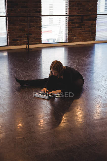 Dancer sitting on floor, stretching and using digital tablet in dance studio — Stock Photo