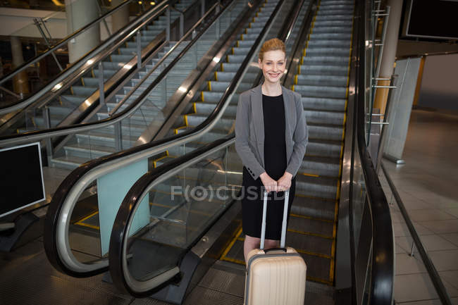 Empresária de pé perto de escada rolante com bagagem no aeroporto — Fotografia de Stock