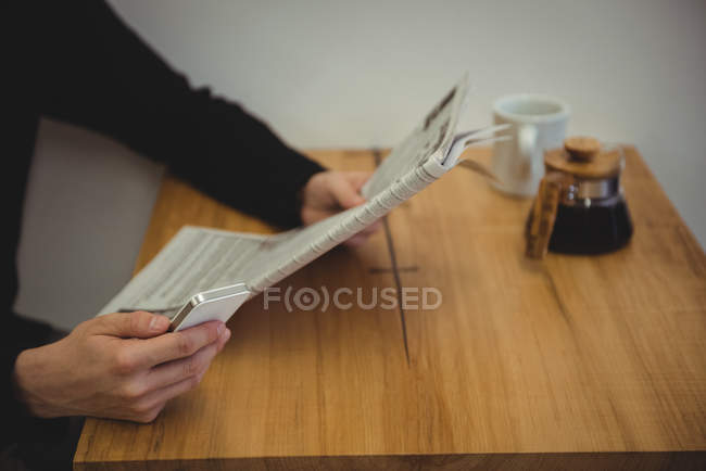 Mid-section of man reading a newspaper in coffee shop — Stock Photo