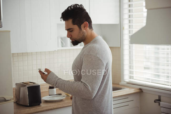 Человек, использующий мобильный телефон на кухне дома — стоковое фото
