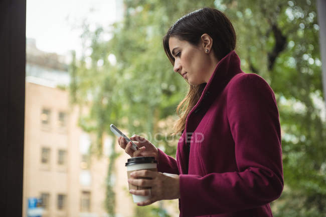Бізнес-леді тримає одноразову чашку кави і використовує мобільний телефон на вулиці — стокове фото
