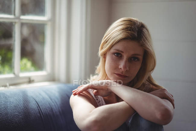 Retrato de una mujer pensativa sentada en un sofá en la sala de estar - foto de stock