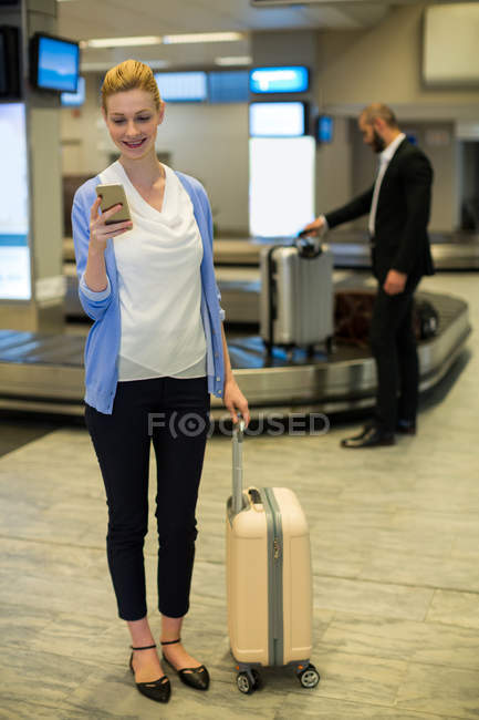Businessman standing with luggage using mobile phone in waiting area at airport terminal — Stock Photo