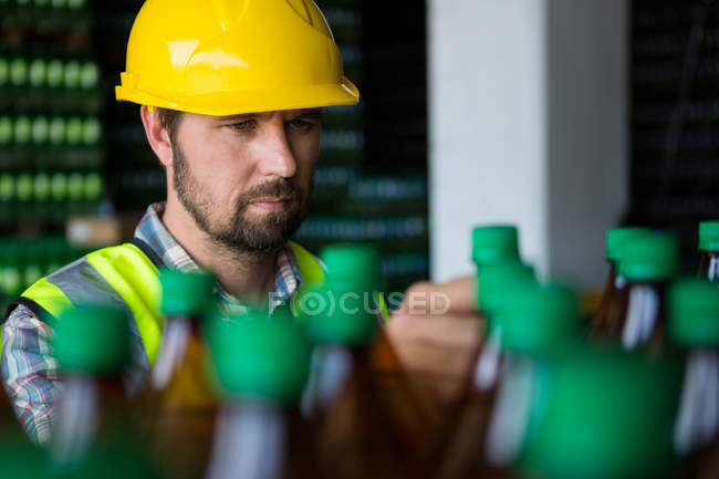 Hombre serio examinando botellas de jugo en la fábrica - foto de stock