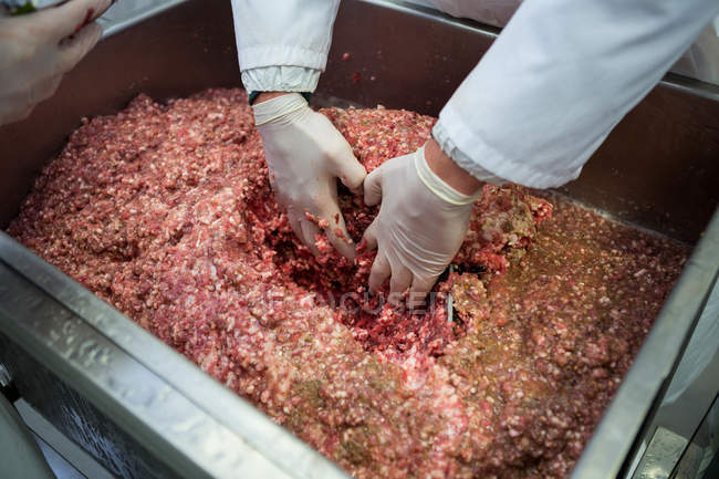 Крупный план рук мясника, смешивающего мясо — стоковое фото