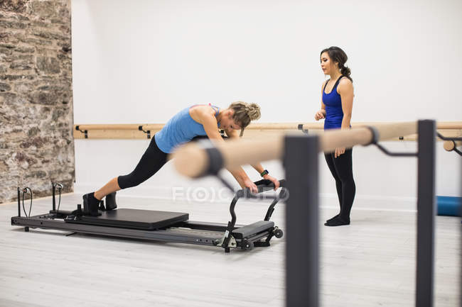 Entraîneur féminin aidant la femme avec l'exercice d'étirement sur le réformateur dans la salle de gym — Photo de stock