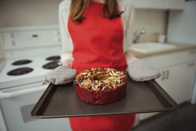 Seção média de mulher em luvas de forno que transportam bolo assado na bandeja — Fotografia de Stock
