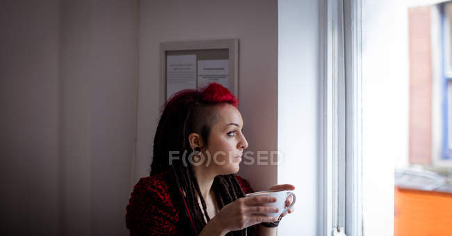 Жінка дивиться крізь вікно, маючи каву в кафе — стокове фото