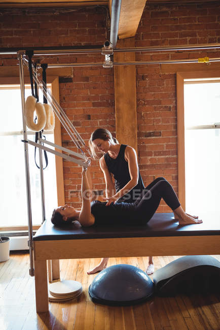 Trainer helping woman while practicing pilates on equipment in fitness studio — Stock Photo