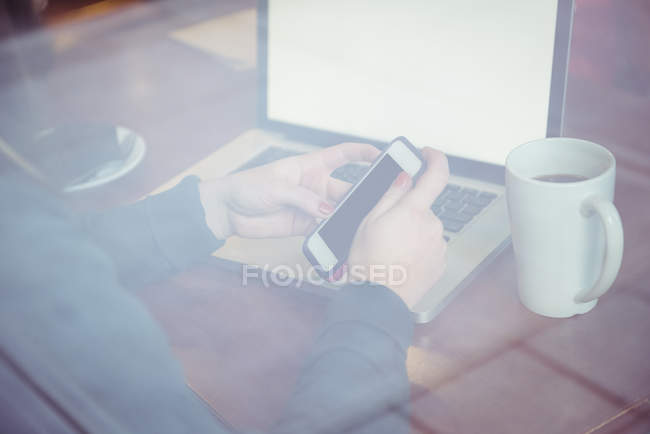 Mujer sentada con taza de café y usando teléfono móvil en el restaurante - foto de stock