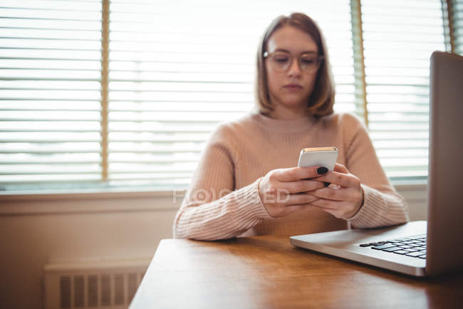 Frau benutzt Handy bei der Arbeit am Laptop zu Hause — Stockfoto