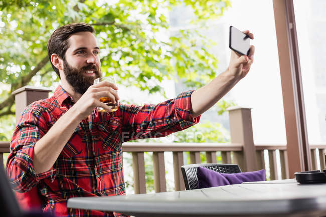 Hombre tomando una selfie mientras toma una copa en el bar - foto de stock