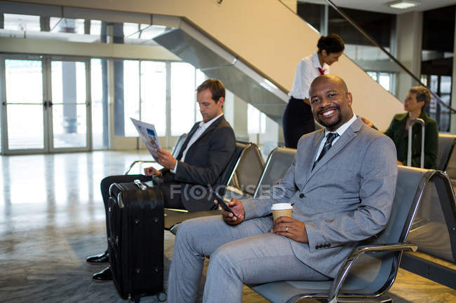 Porträt eines Geschäftsmannes, der sein Handy im Wartebereich des Flughafenterminals benutzt — Stockfoto