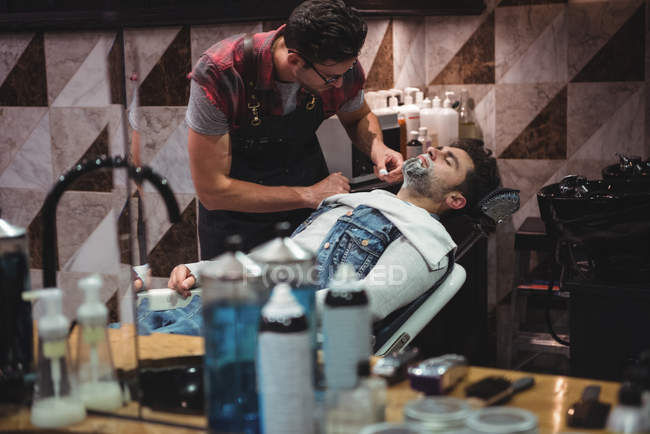 Reflection of man getting beard shaved by hairdresser with razor in barber shop — Stock Photo