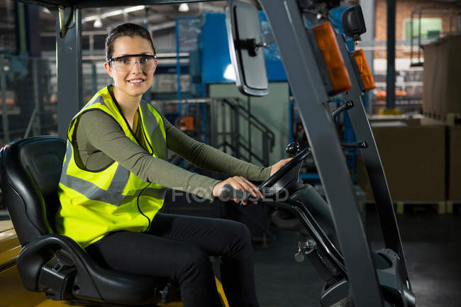 Portrait of beautiful female worker driving forklift in warehouse — Stock Photo
