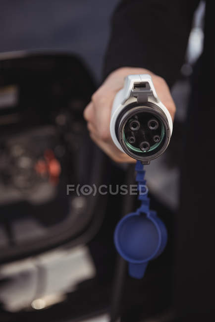 Close-up of man holding car charger at electric vehicle charging station — Stock Photo