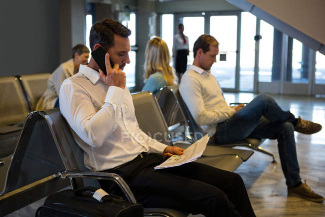 Empresario hablando por teléfono móvil en la sala de espera en la terminal del aeropuerto - foto de stock