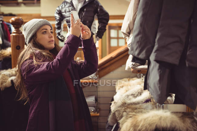 Женщина фотографирует одежду с помощью мобильного телефона в магазине одежды — стоковое фото