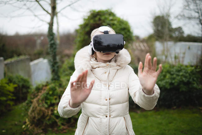 Mujer con abrigo de furia usando auriculares de realidad virtual al aire libre - foto de stock