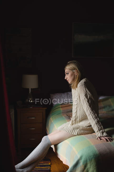 Mujer sentada en la cama en el dormitorio - foto de stock