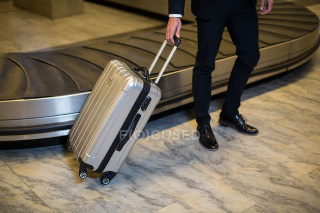 Low section of businessman standing with trolley bag in waiting area — Stock Photo