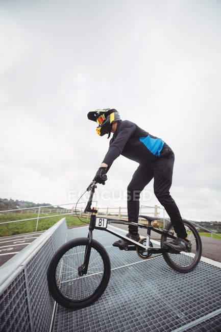 Велогонщик готовится к гонкам BMX на старте пандуса в скейтпарке — стоковое фото