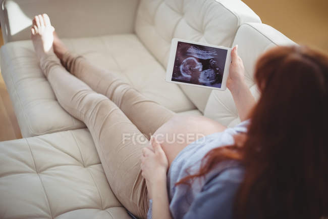 Вагітна жінка дивиться на сонографію на цифровому столі у вітальні — стокове фото