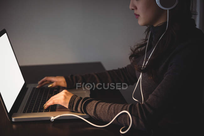 Frau hört Kopfhörer, während sie zu Hause im Arbeitszimmer Laptop benutzt — Stockfoto
