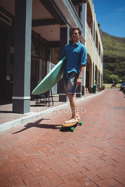 Uomo che trasporta tavola da surf mentre cavalca skateboard anche se sentiero — Foto stock