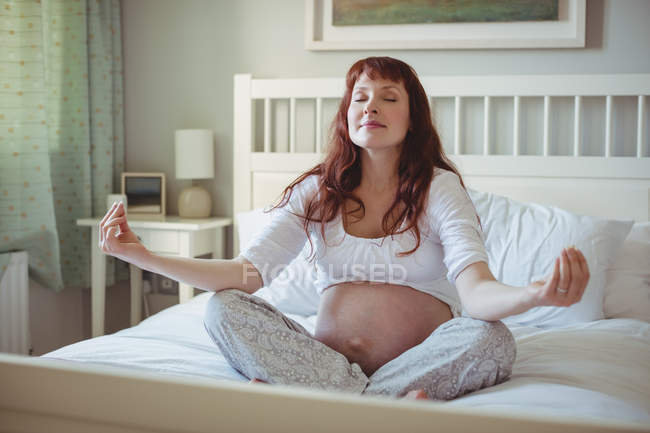 Mulher grávida realizando ioga na cama no quarto — Fotografia de Stock