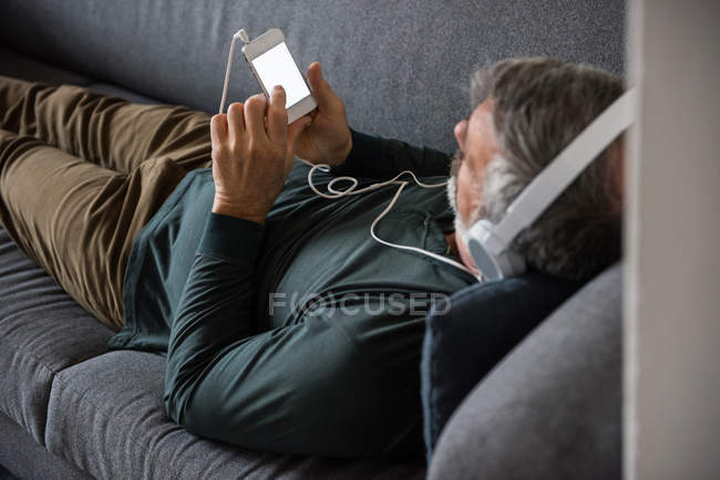 Человек слушает музыку на мобильном телефоне дома — стоковое фото