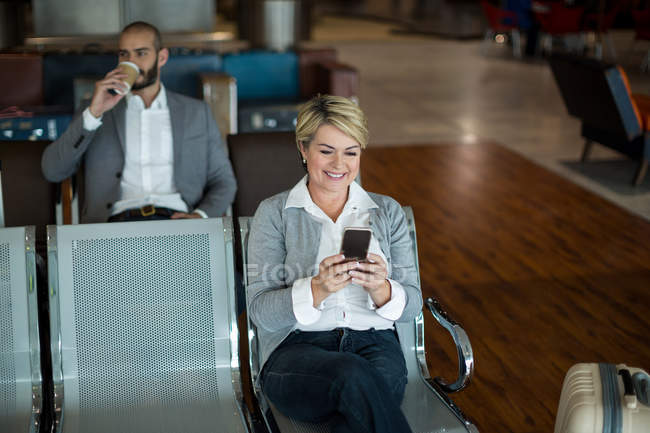 Усміхнена бізнес-леді, використовуючи мобільний телефон в зоні очікування в терміналі аеропорту — стокове фото