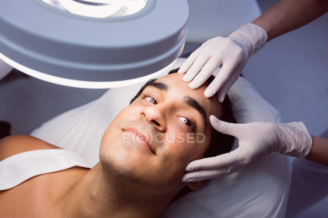 Hände des Arztes untersuchen männliches Gesicht für kosmetische Behandlung in Klinik — Stockfoto