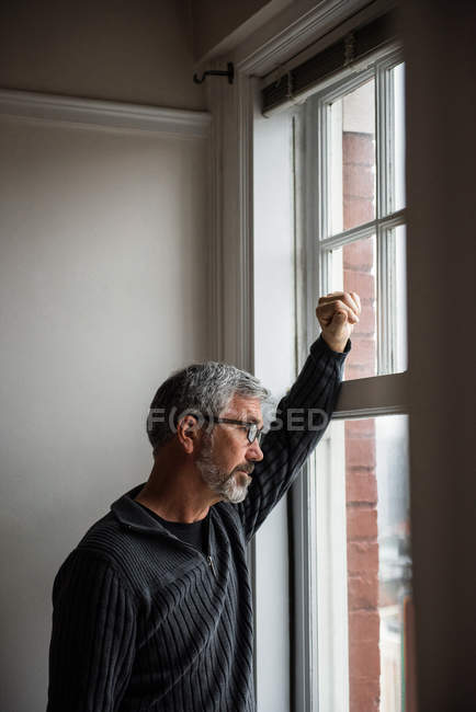 Uomo premuroso che guarda attraverso la finestra a casa — Foto stock