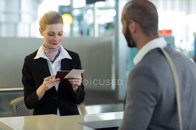 Caminante parado en el mostrador mientras el asistente revisa su pasaporte en la terminal del aeropuerto - foto de stock