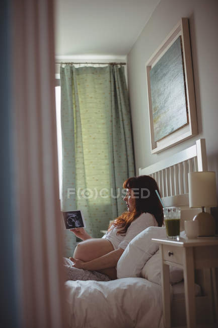 Pregnant woman looking at a sonography on digital table in bedroom — Stock Photo