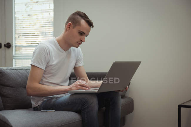 Молодий чоловік використовує ноутбук на дивані вдома — стокове фото