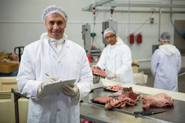 Retrato de açougueiro macho mantendo registros na área de transferência na fábrica de carne — Fotografia de Stock