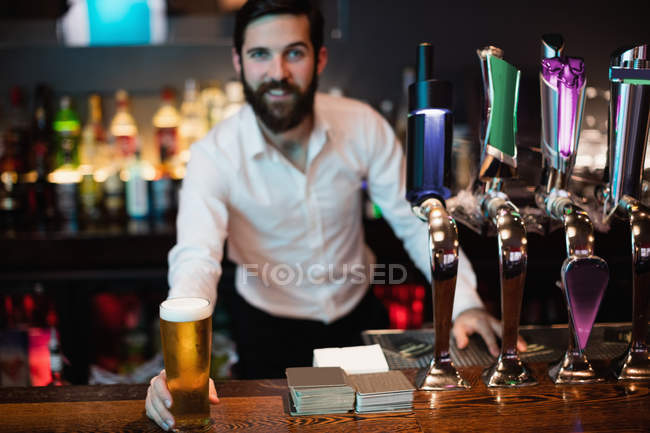 Cantinero macho sosteniendo vaso de cerveza en el mostrador del bar - foto de stock