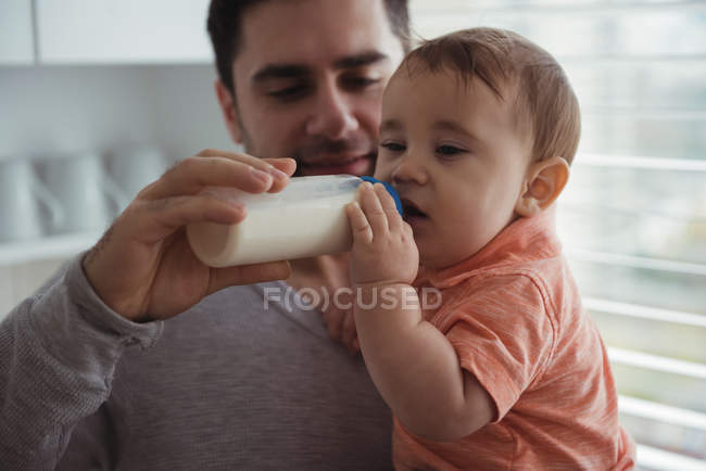 Padre che nutre il bambino con la bottiglia di latte in cucina — Foto stock